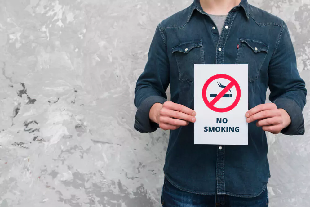 Young man holding no smoking text and sign poster over old wall