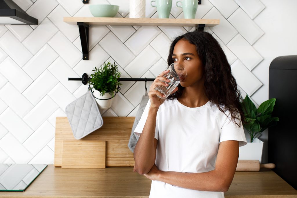 African girl stands in kitchen drinking water
