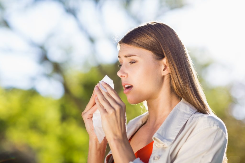 young woman outside sneezing from tree pollen allergy.