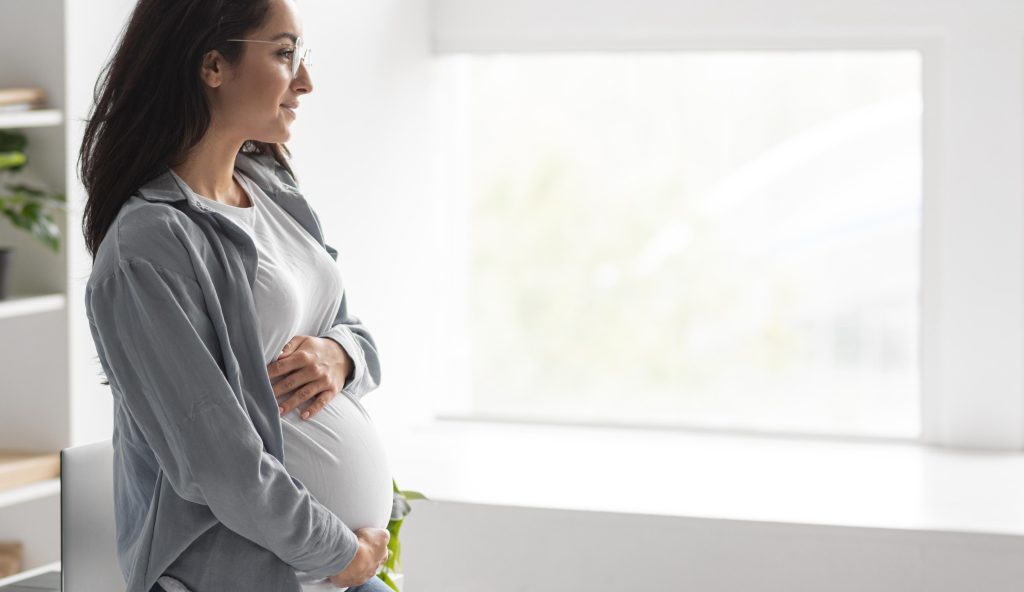 woman looking out the window holding her belly happy to be pregnant