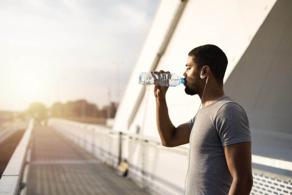 young athletic man outside training drinking water
