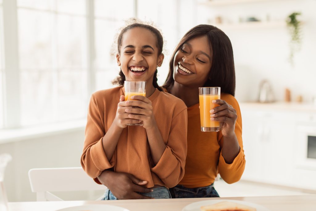 happy beautiful mother and daughter enjoying fresh orange juice in their kitchen 