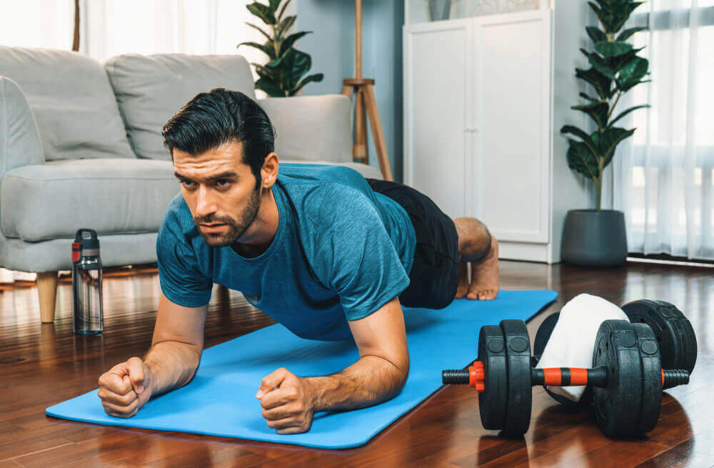 Athletic and sporty man doing plank on fitness mat at gaiety home