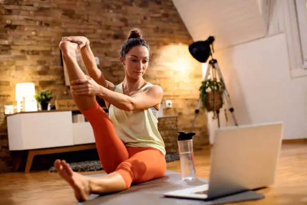 Female athlete stretching her leg while using laptop at home