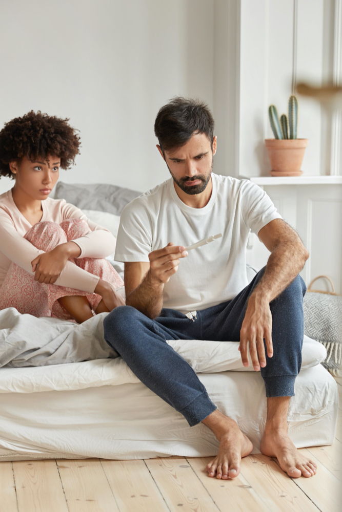 Desperate mixed race couple finds out about unwanted pregnancy, look with sad expression at test.