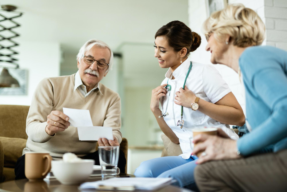 Happy mature couple showing their photos to a female doctor who is visiting them at home focus is on doctor