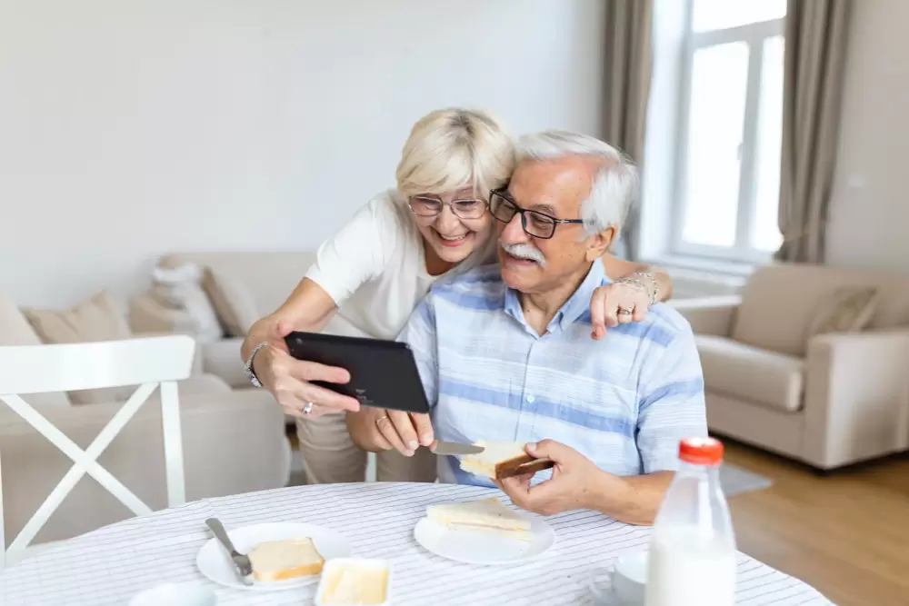 Happy old family couple talking with grandchildren using tablet surprised excited senior woman looking at tablet waving and smiling