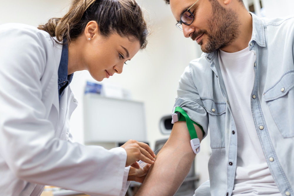 Friendly hospital phlebotomist collecting blood sample from patient in lab preparation for blood test by female doctor 