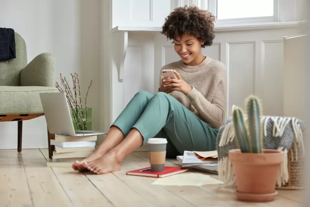 positive attractive black lady holding smart phone while drinking coffee at home. 