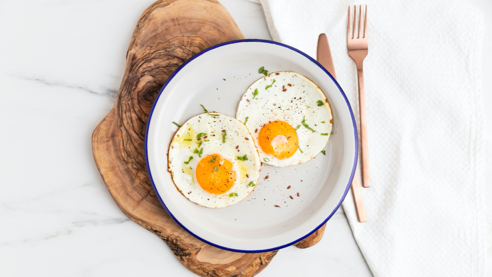 Top view of breakfast fried eggs on plate with cutlery