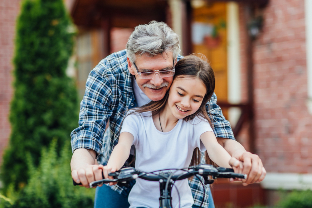 First lessons bicycle riding. handsome grandather teach his granddaughter to ride a bike. practicing near home.