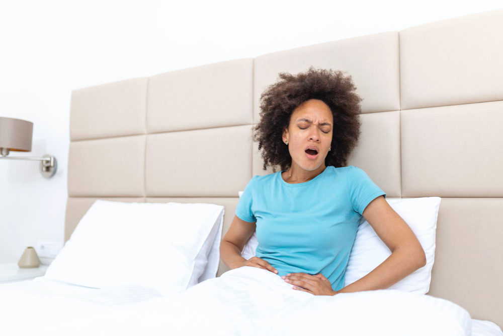 photo woman in painful expression holding hands against belly suffering menstrual period pain lying sad on home bed 