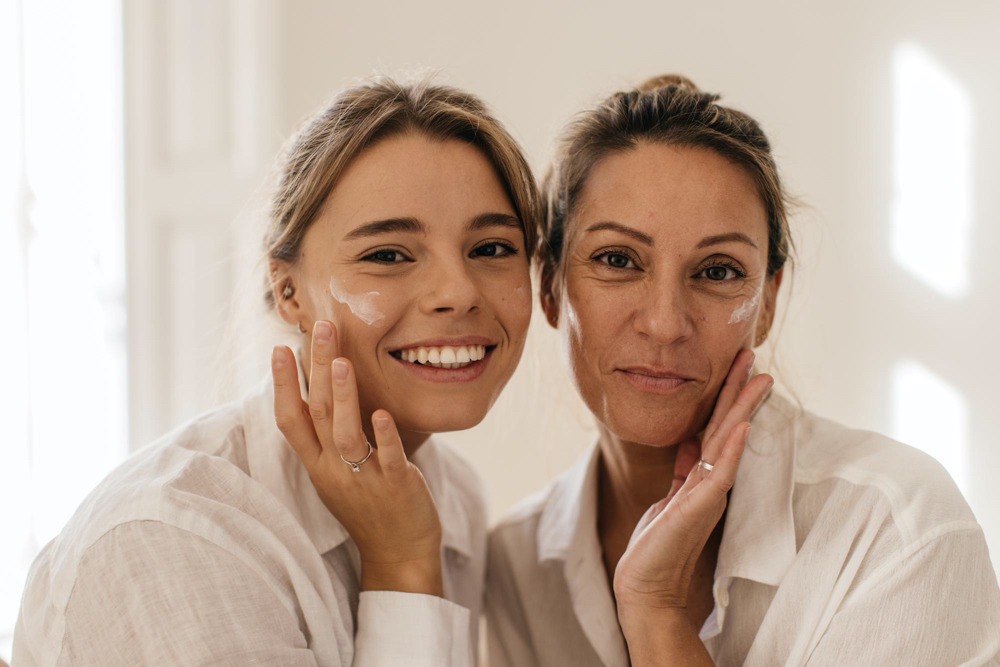 photo close-up of two cute caucasian women smearing their face with cream and looking at camera