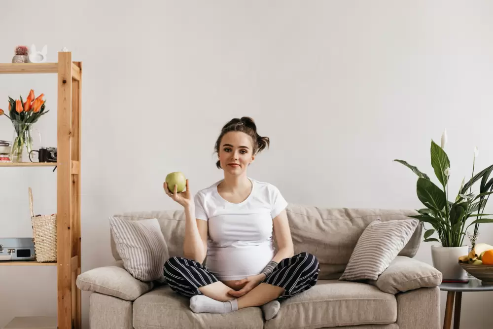 photo cool young pregnant woman in white tee and striped pants holds green apple