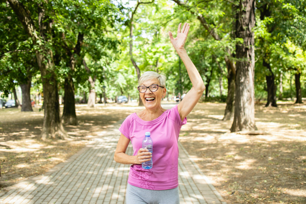 Photo smiling senior caucasian woman waving to her friend while jogging in the park.