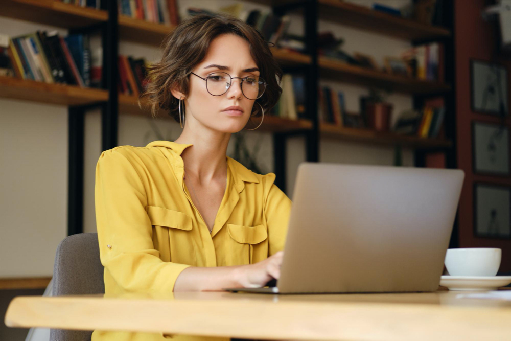 photo young serious businesswoman in eyeglasses sitting at the desk thoughtfully working on new project with laptop 