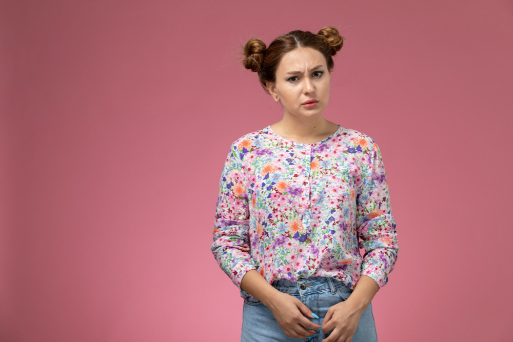 photo front view young female in flower designed shirt and blue jeans just posing on the pink background
