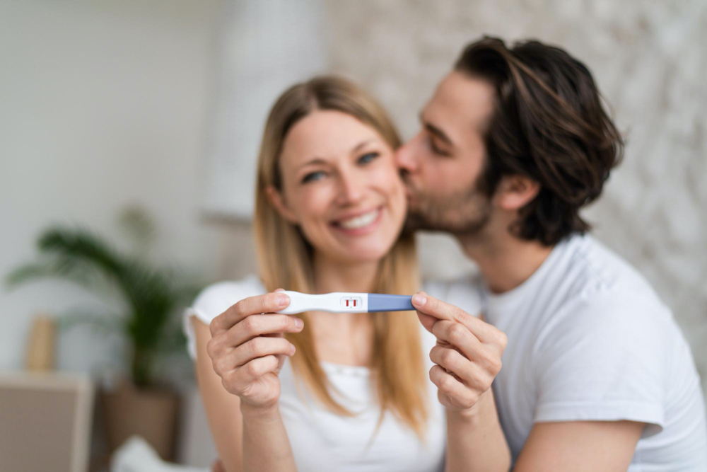 happy young couple showing positive pregnancy test and kissing at home selective focus
