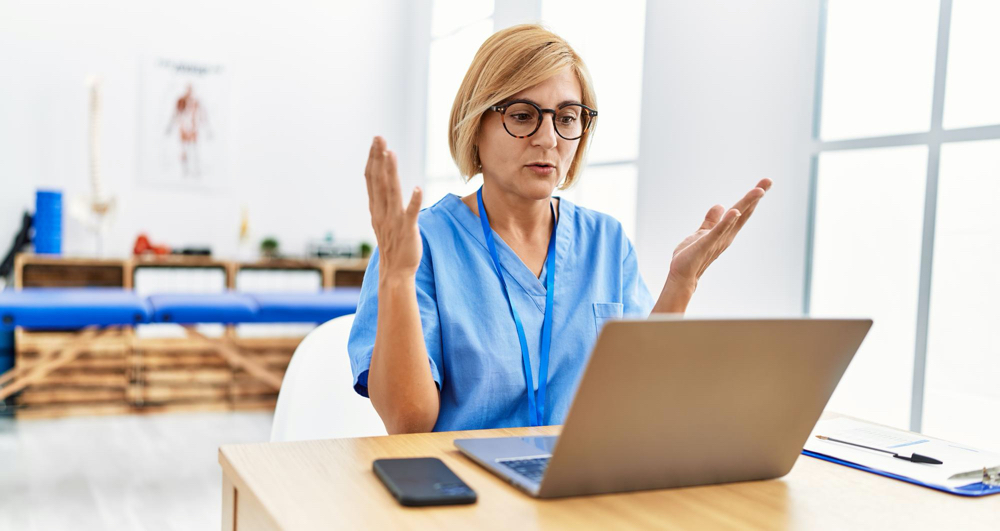 middle age blonde woman wearing physio therapy uniform having video call at clini