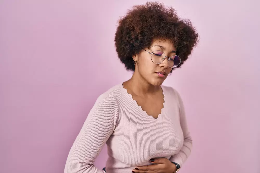 Free photo young african american woman standing over pink background with hand on stomach because indigestion, painful illness feeling unwell. ache concept.
