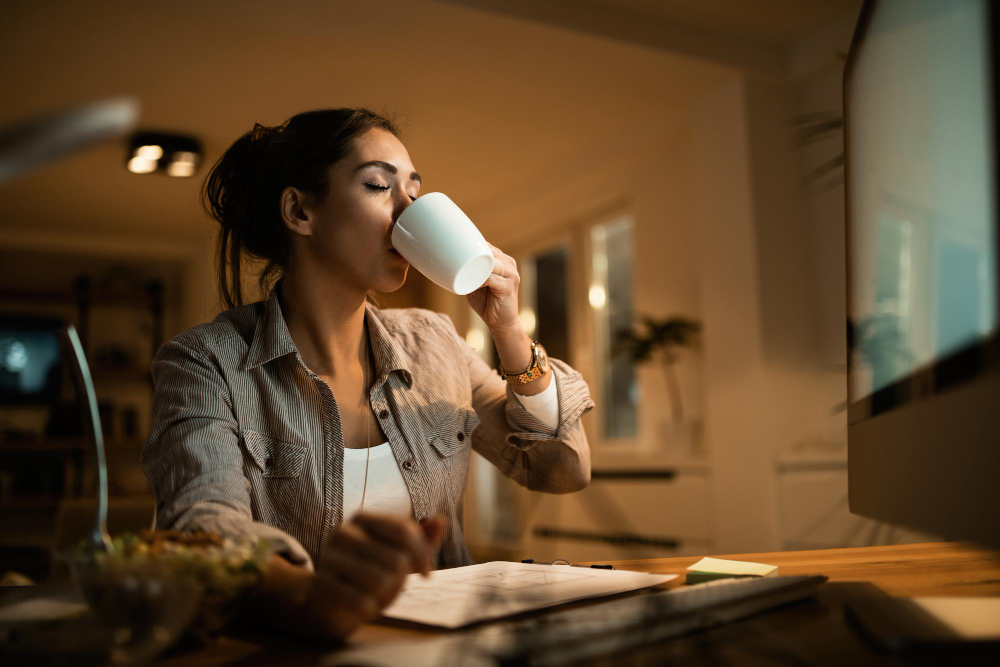 Free photo young woman drinking coffee with eyes closed while studying at night at home