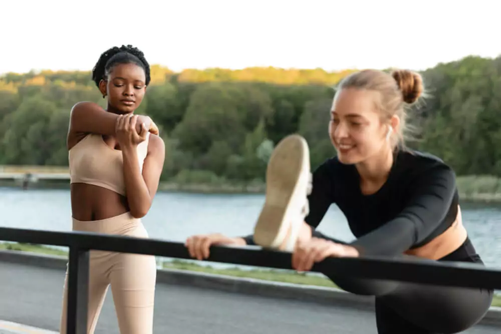 horizontal shot of two athletic women stretching their legs and back outside on a sunny day. 