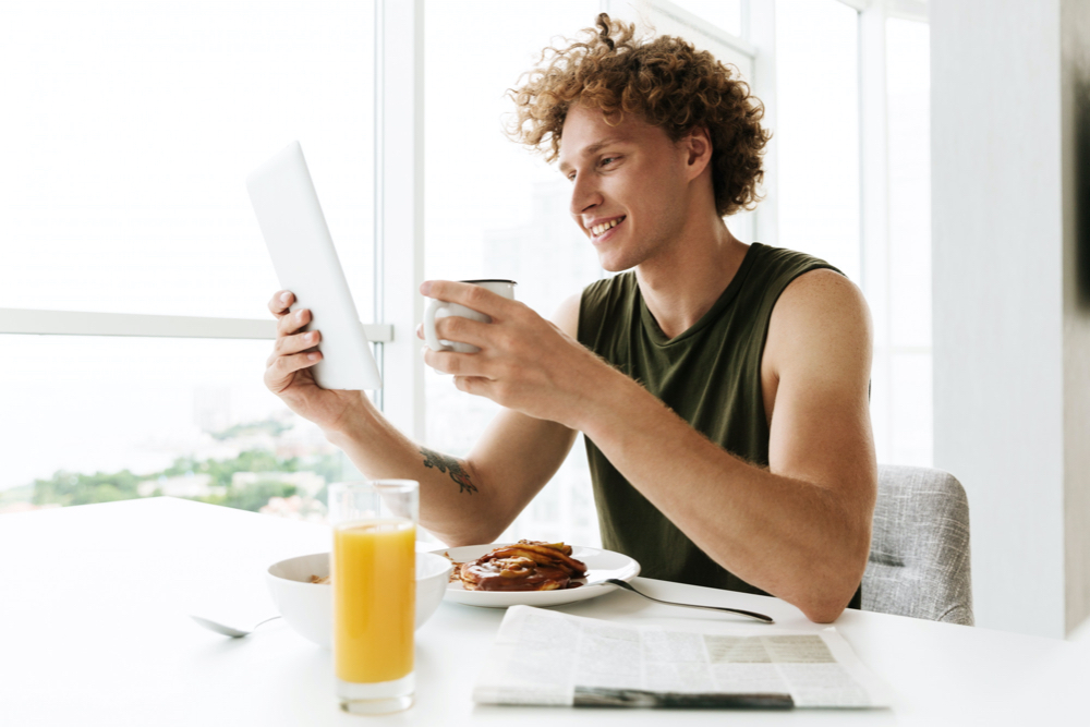 handsome happy man using tablet computer and drinking coffee