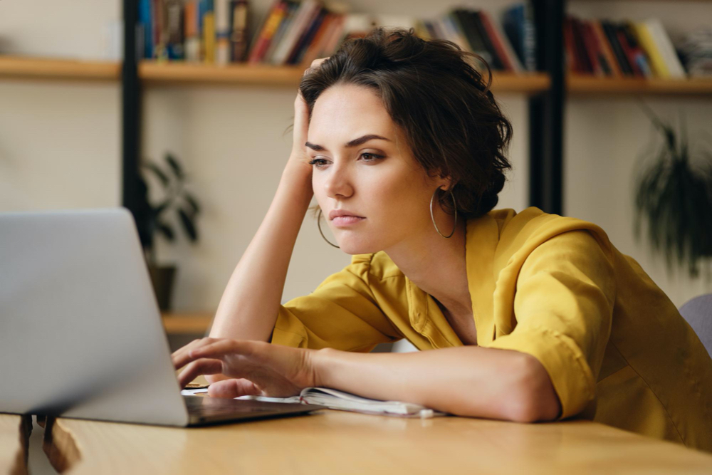 Free photo young upset woman sitting at the desk tiredly working on new project with laptop in modern office
