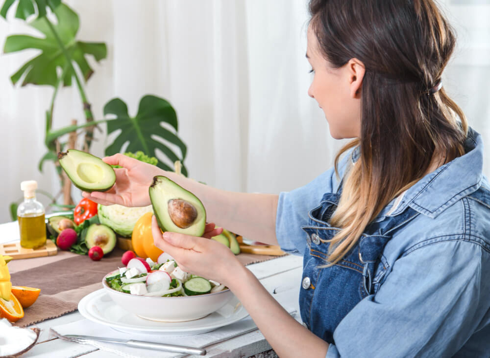 Young and happy woman looking at the avocado at the dinner table